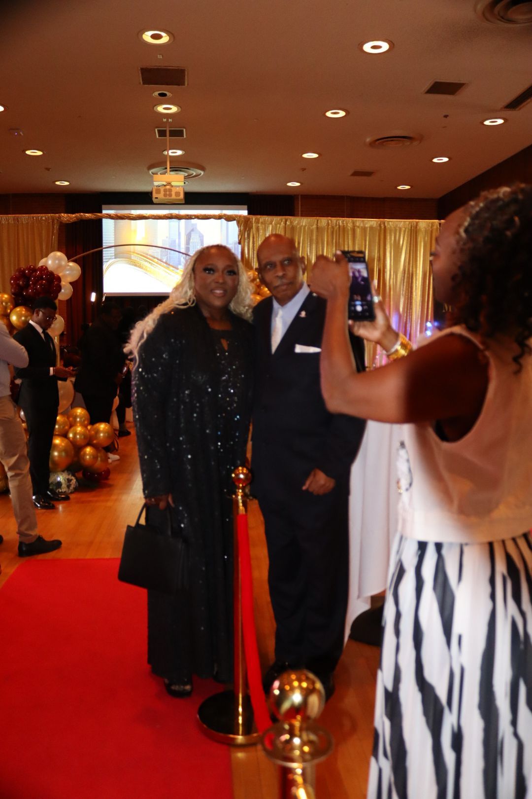 A woman is taking a picture of a man and woman on a red carpet.
