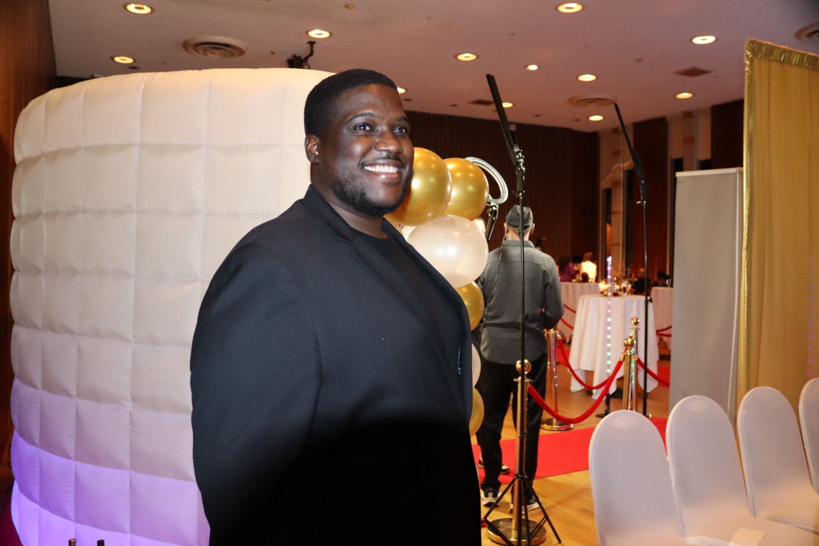 A man in a black suit is standing in front of a white inflatable cube.