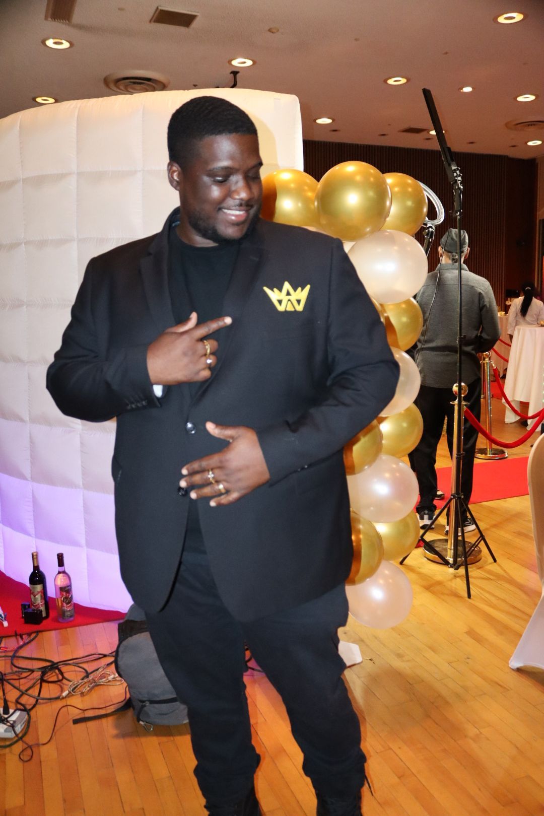 A man in a black suit is standing in front of balloons.