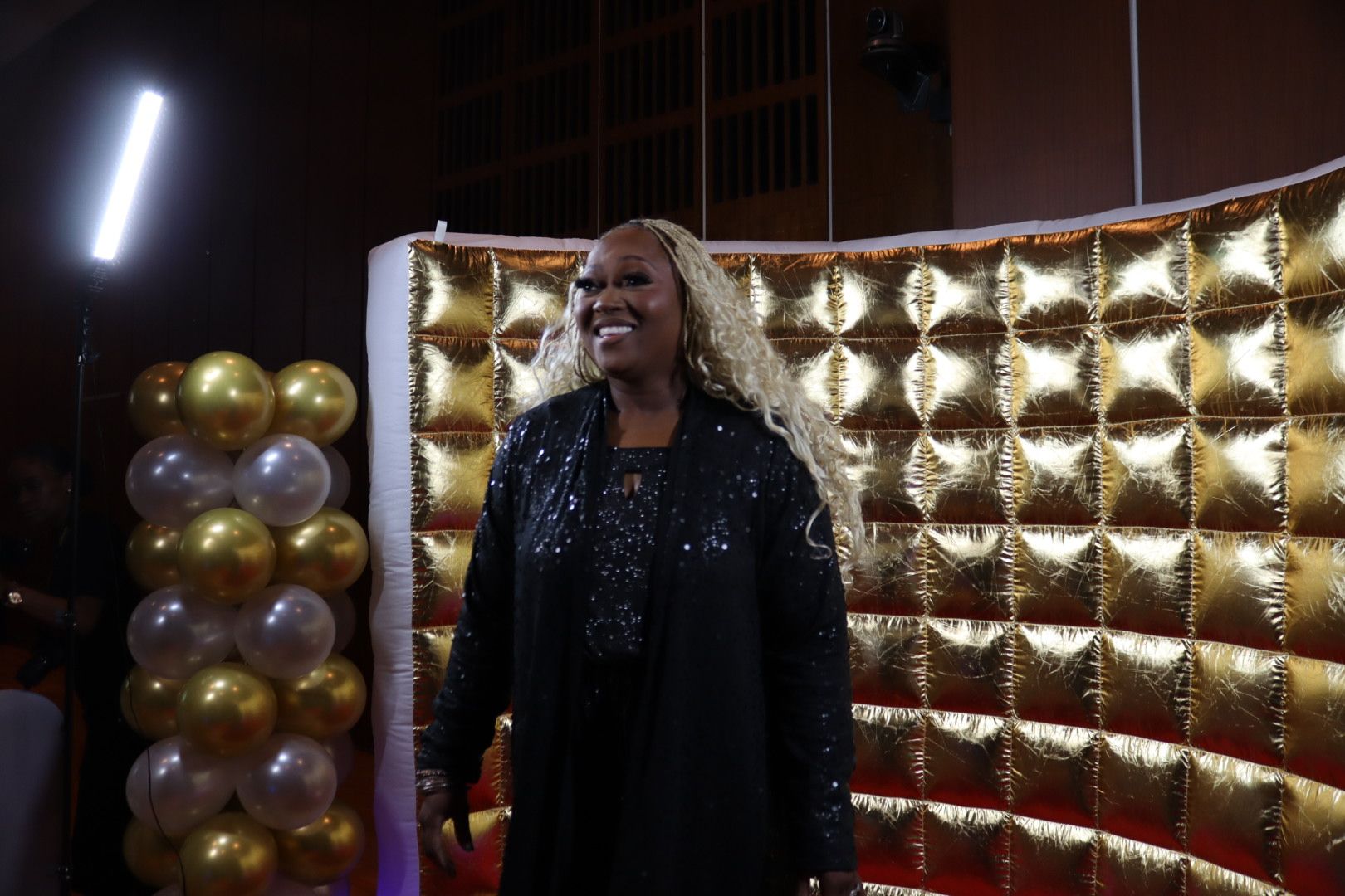 A woman is standing in front of a gold wall with balloons.