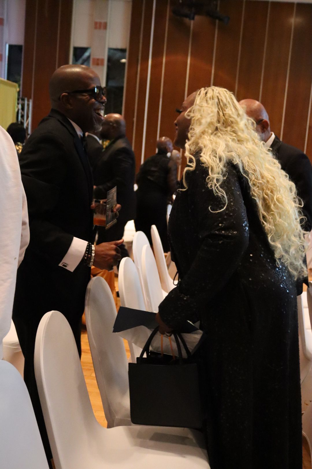 A woman with blonde hair is sitting in a chair talking to a man in a suit