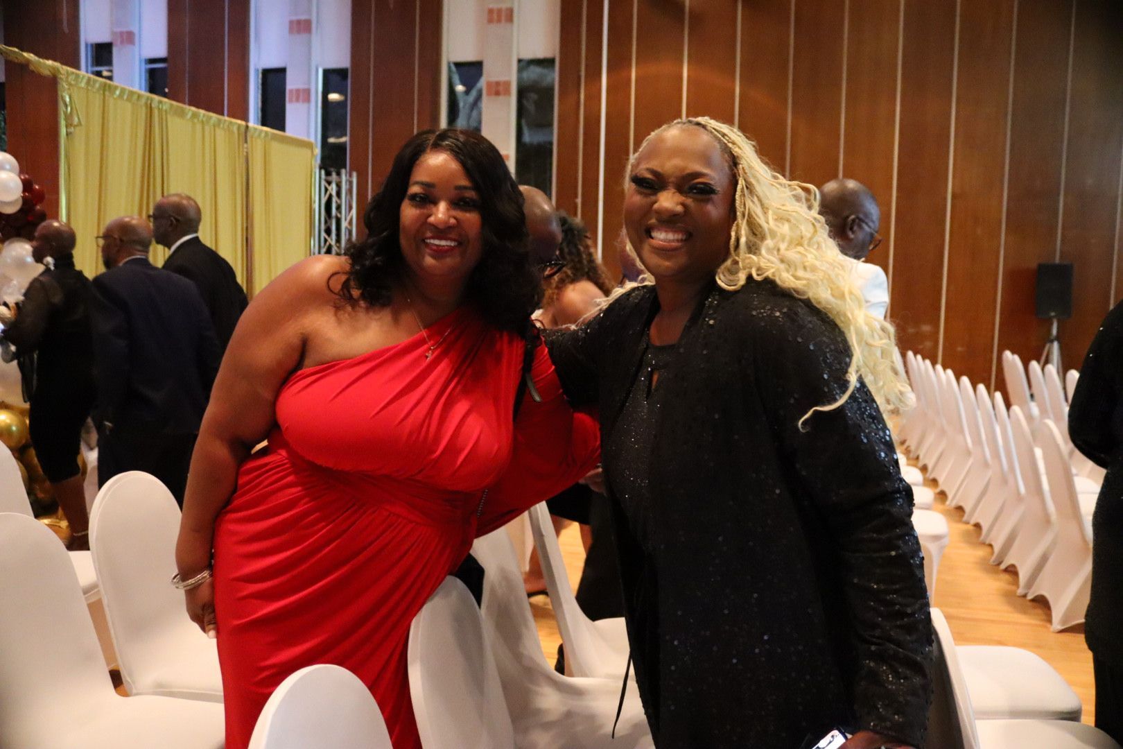 Two women posing for a picture in a room with chairs