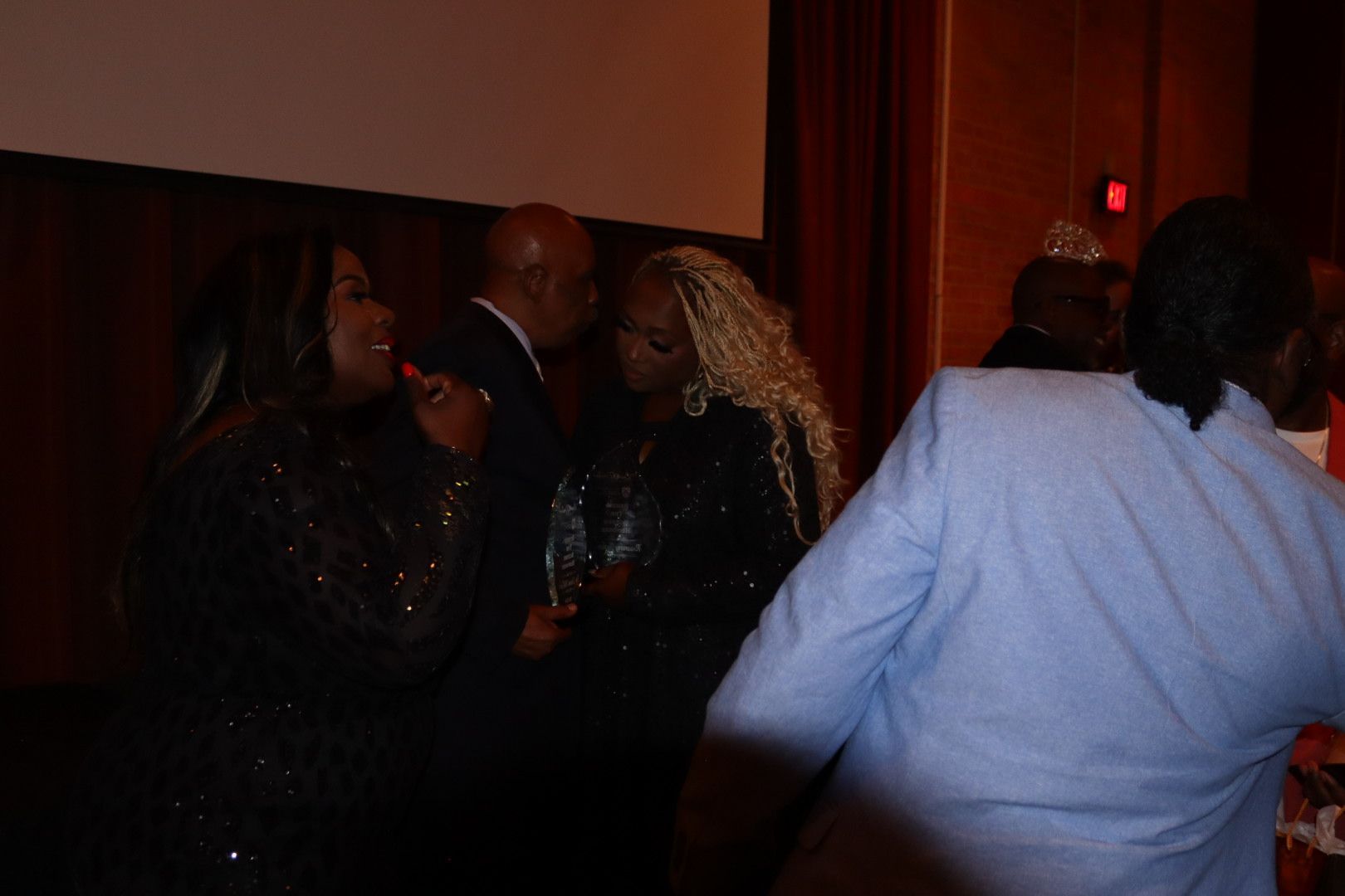 A group of people are standing in a dark room talking to each other.