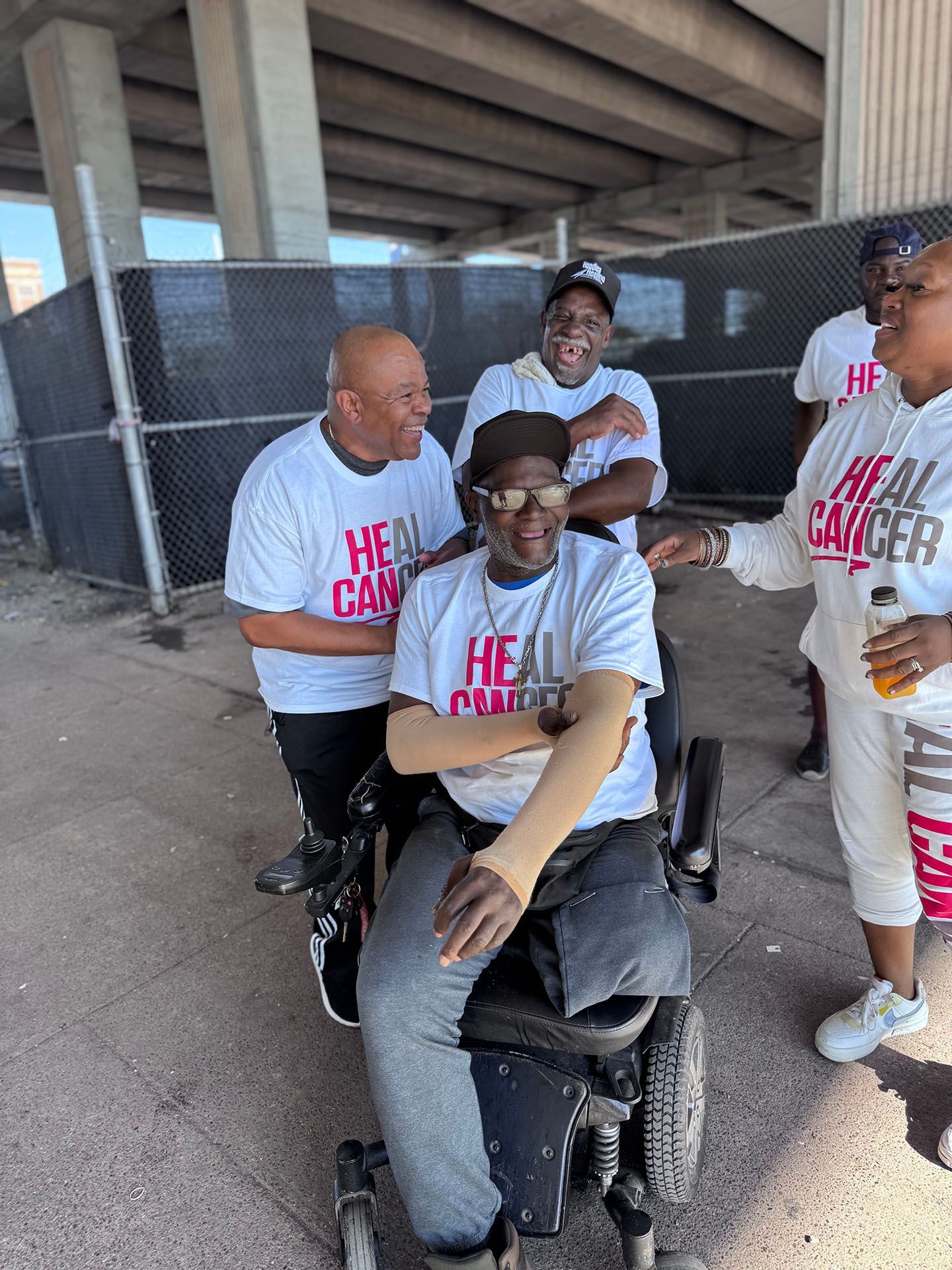 A group of people are standing around a man in a wheelchair.