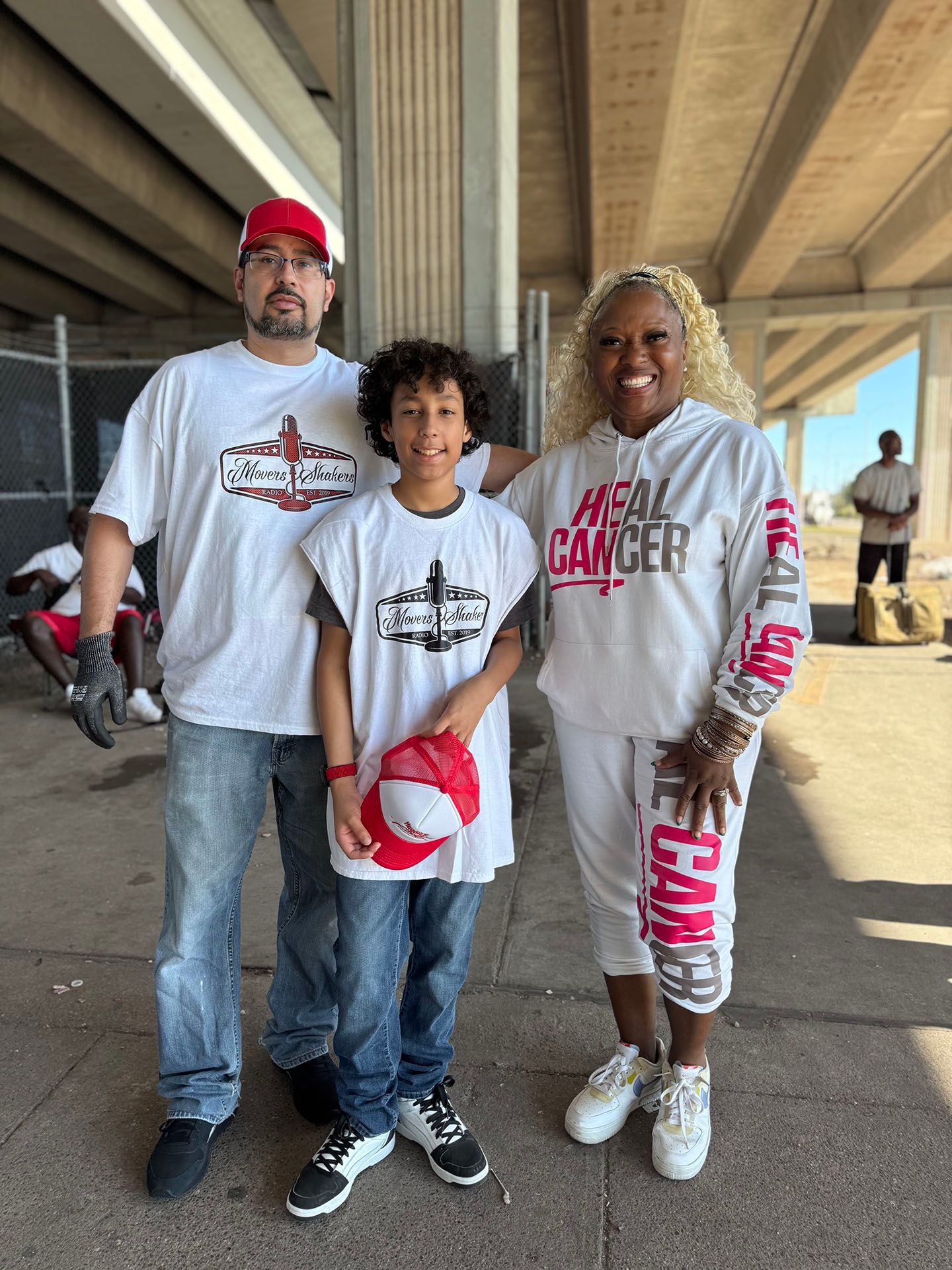 A man , a woman and a boy are posing for a picture under a bridge.