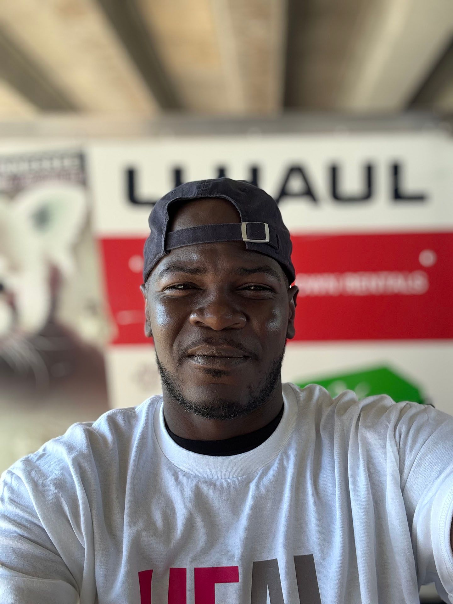 A man wearing a hat and a white shirt is taking a selfie in front of a uhaul truck.