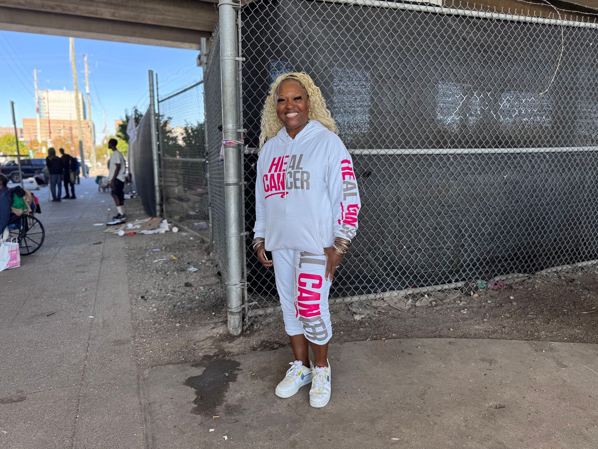 A woman wearing a hoodie and shorts is standing in front of a chain link fence.