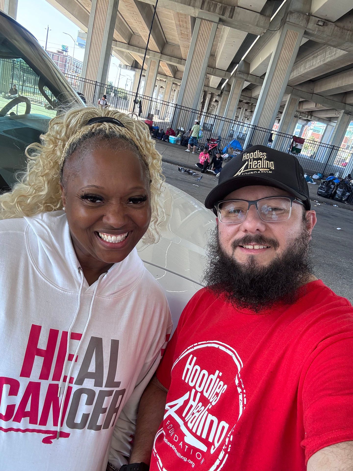 A man and a woman are posing for a picture . the woman is wearing a hoodie that says `` heal cancer ''.