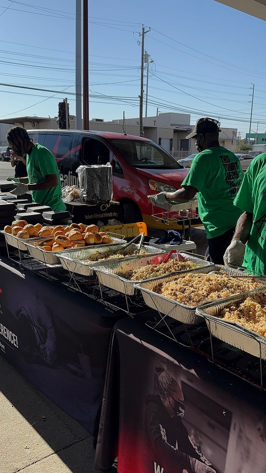 A group of people are standing around a table filled with trays of food.