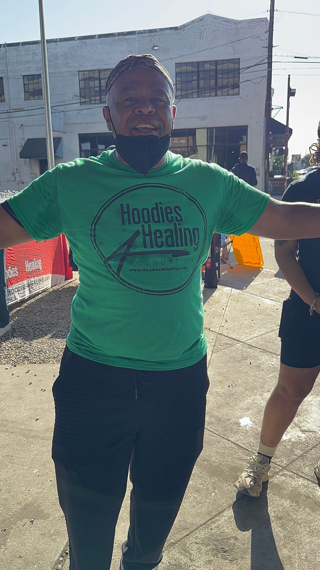 A man wearing a green t-shirt is standing on a sidewalk with his arms outstretched.
