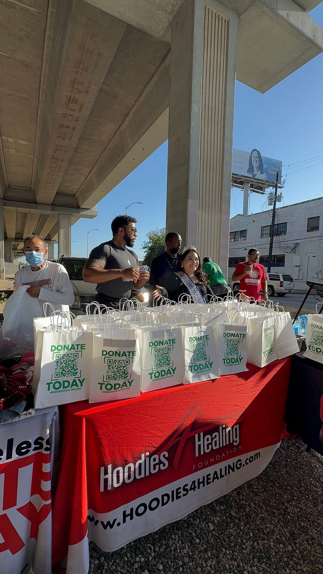 A group of people are standing around a table with bags on it.