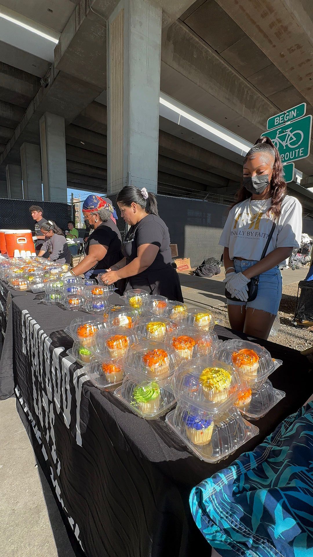 A group of people are standing around a table filled with cupcakes.