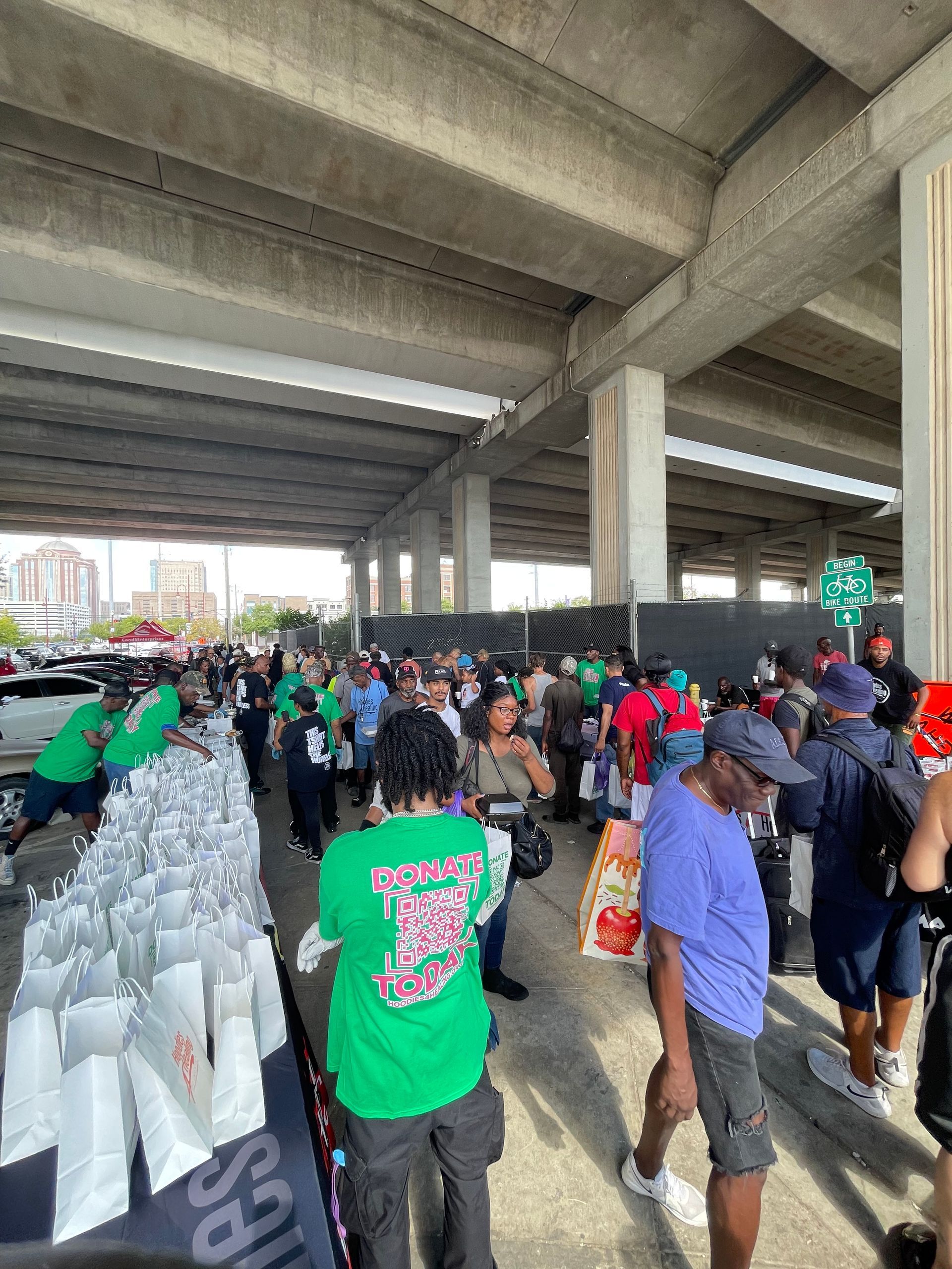 A group of people are standing in a parking lot under a bridge.