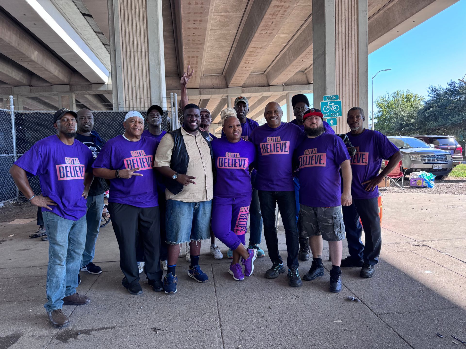 A group of people wearing purple shirts are posing for a picture under a bridge.