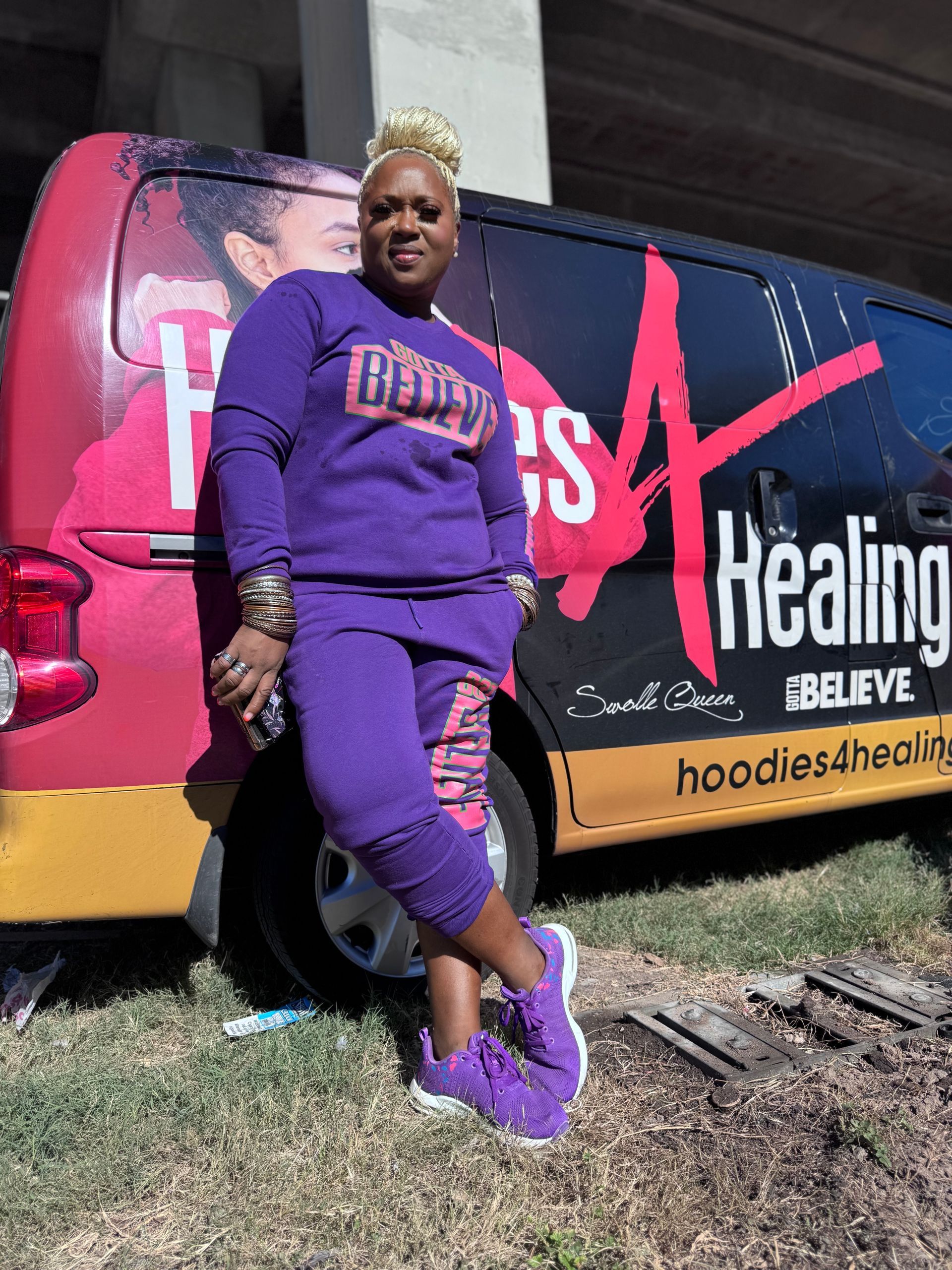 A woman in a purple outfit is standing in front of a healing van.