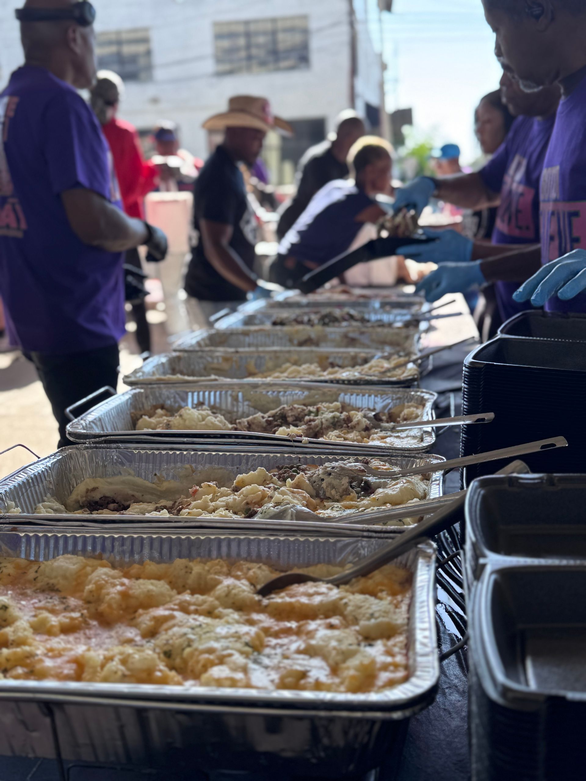 A group of people are standing around a table filled with trays of food.