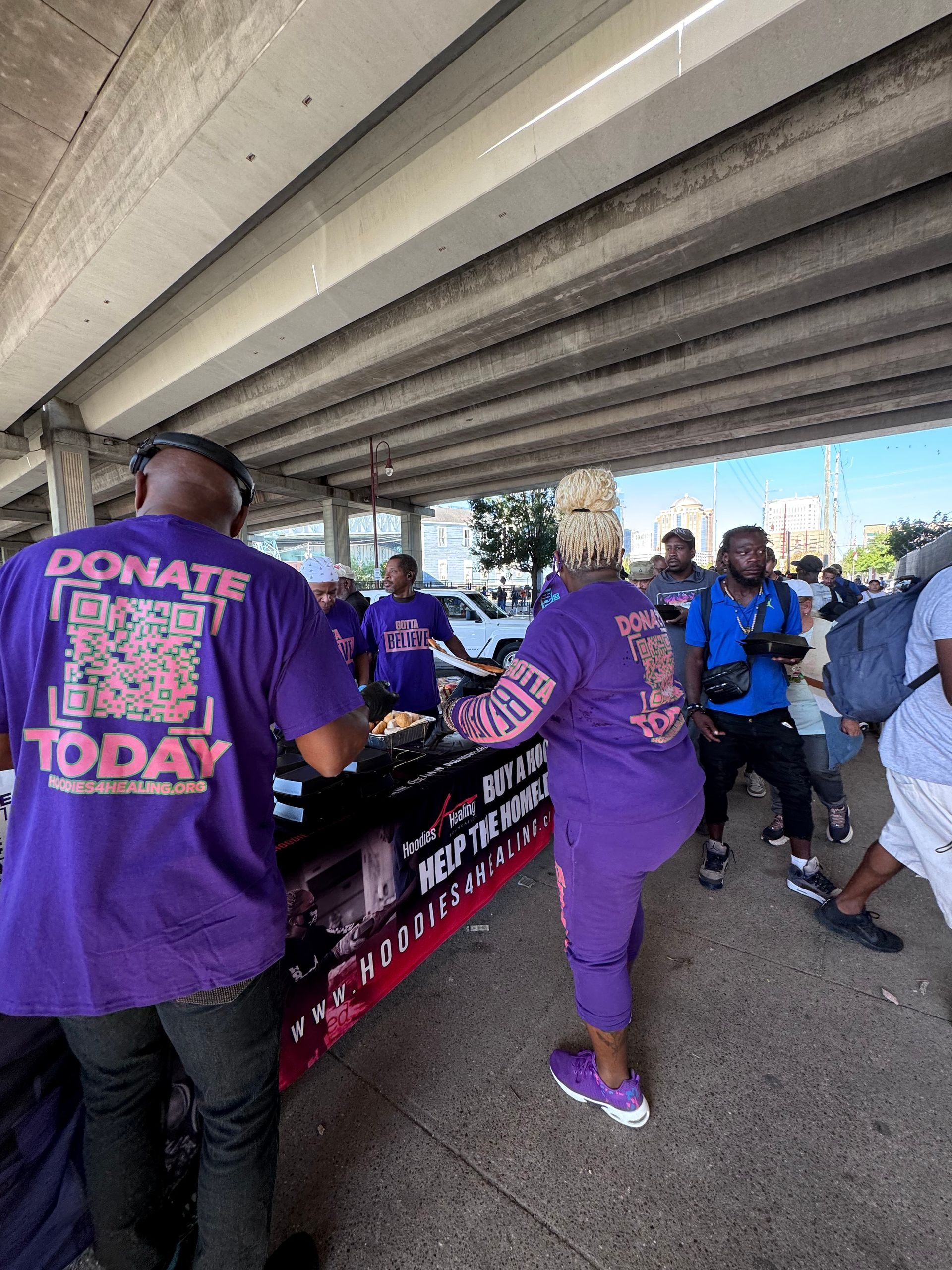 A group of people are standing around a table under a bridge.