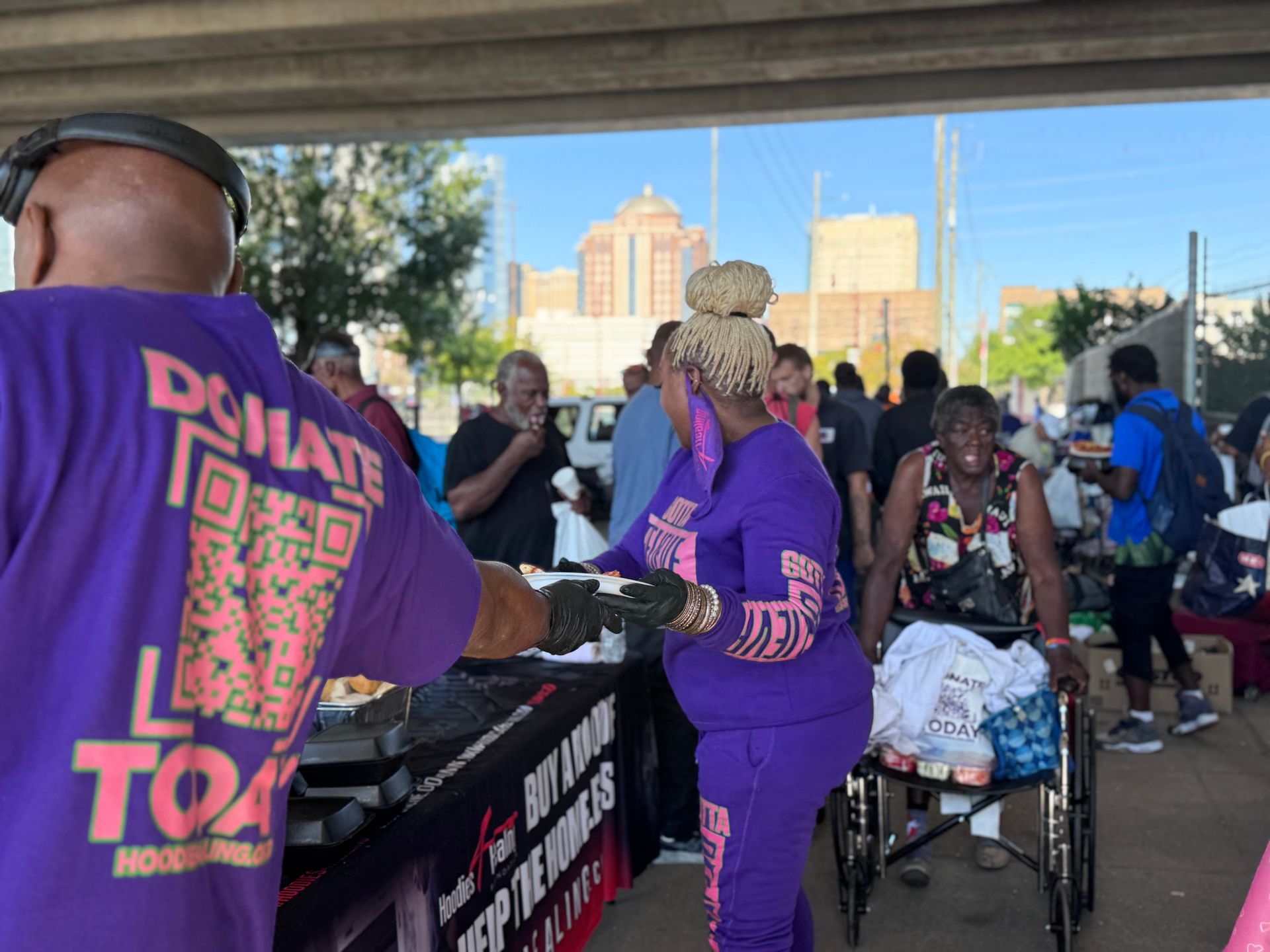 A man wearing a purple shirt that says donate to a lady in a wheelchair