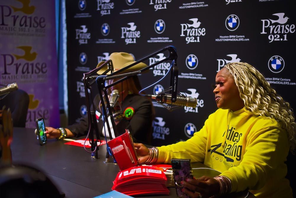 A woman in a yellow sweatshirt is sitting at a table in front of a microphone.