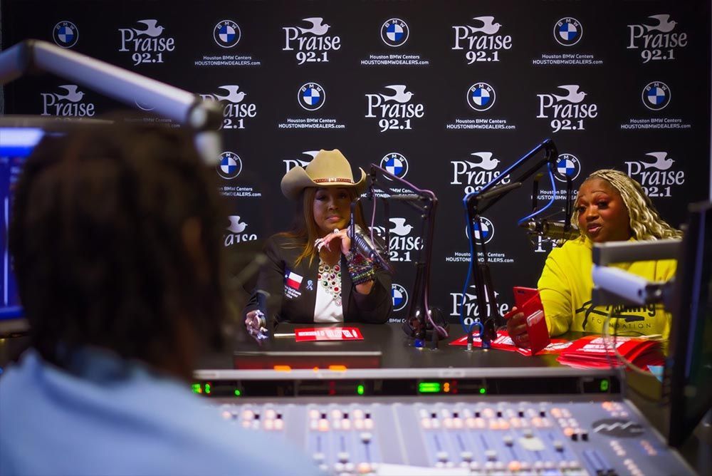 A woman in a cowboy hat is talking into a microphone in a radio studio.