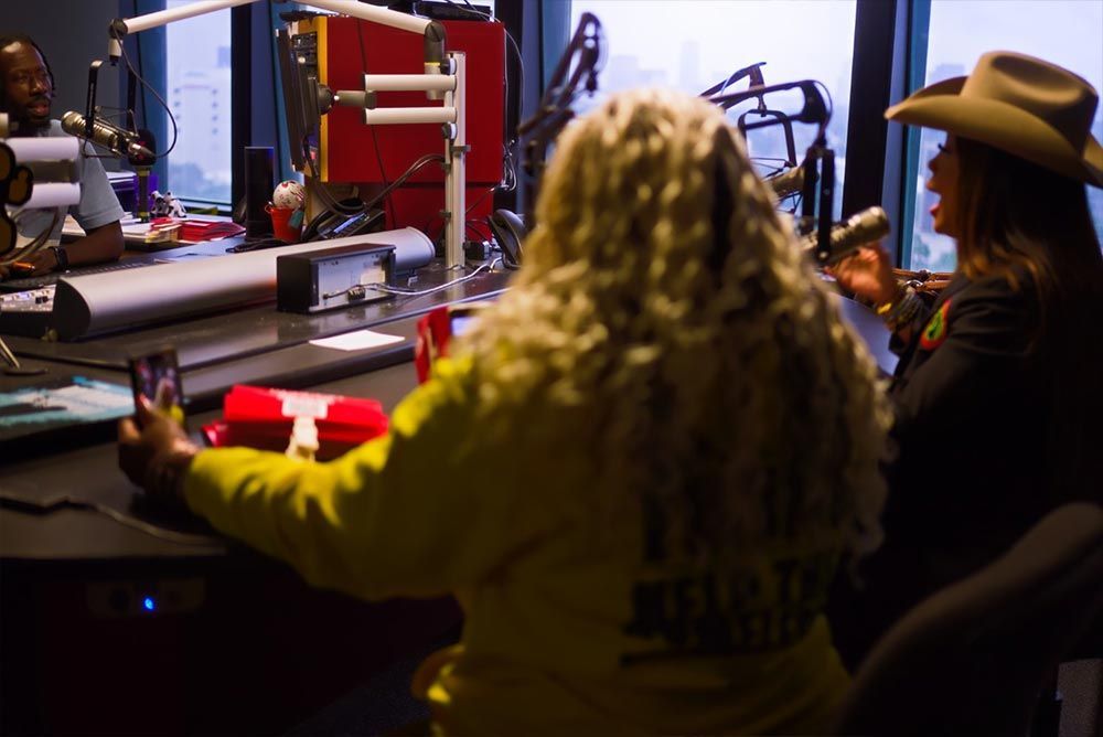 Two women are sitting in front of microphones in a radio studio.