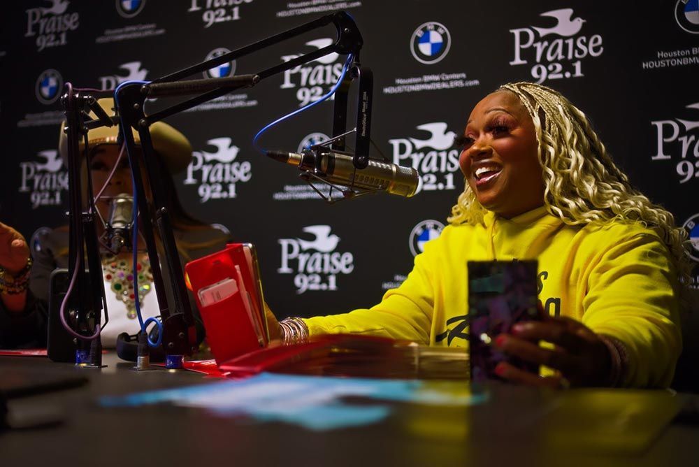 A woman in a yellow sweatshirt is sitting at a table in front of a microphone.