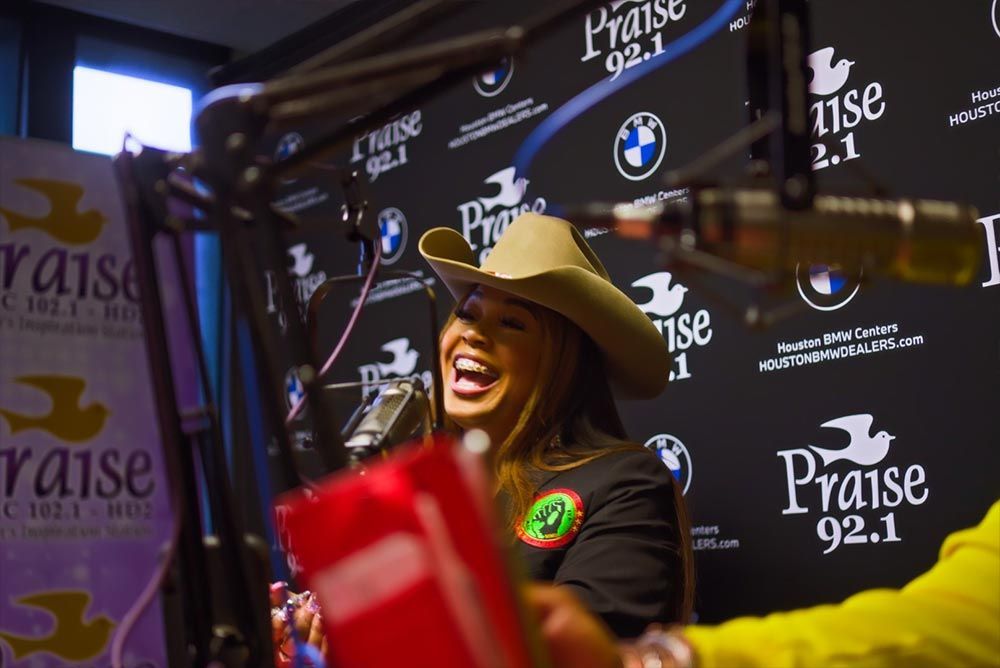 A woman in a cowboy hat is laughing in front of a microphone at praise 92.1