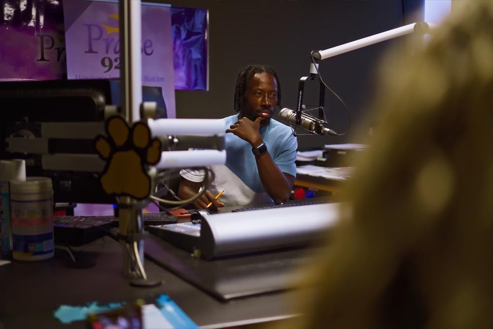 A man is sitting at a desk in front of a microphone.