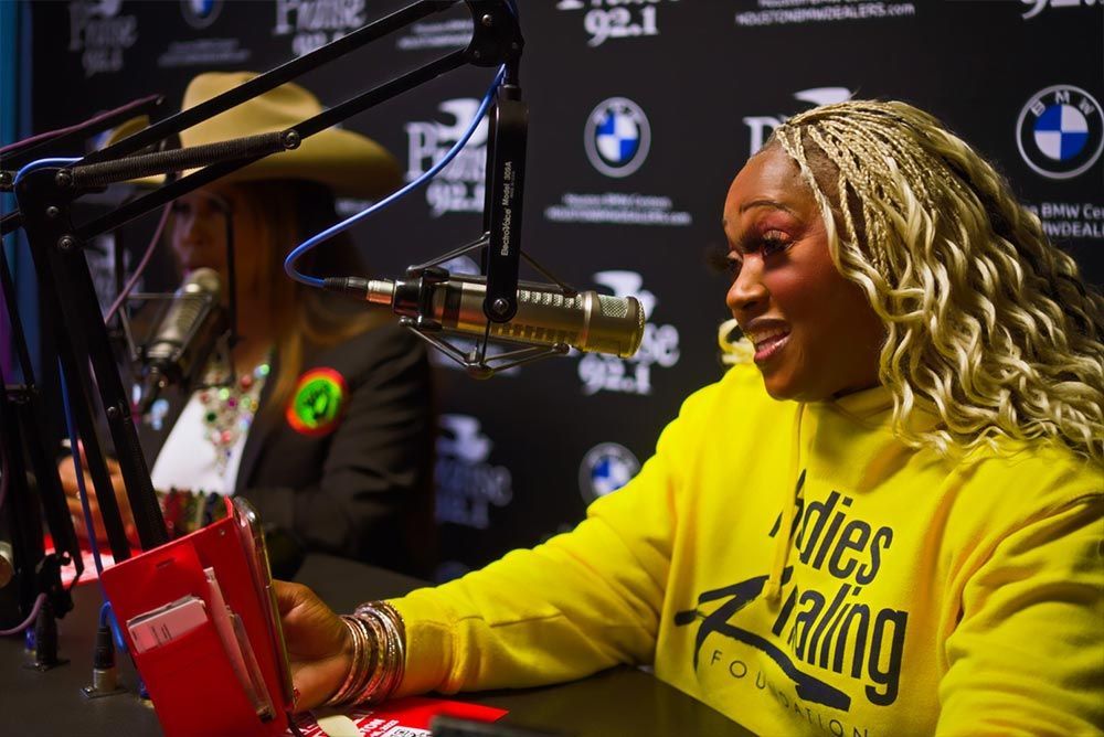 A woman in a yellow hoodie is sitting in front of a microphone.