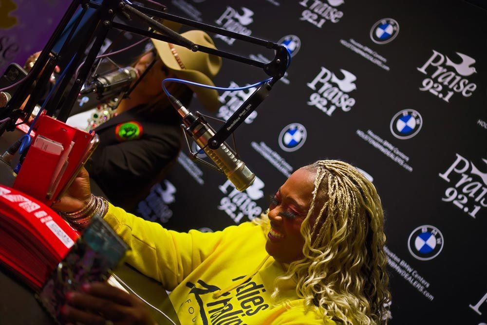 A woman in a yellow shirt is sitting in front of a microphone at praise 92.1