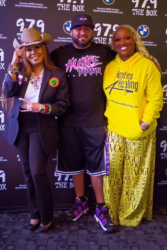 Three people posing for a picture in front of a wall that says 979 the box