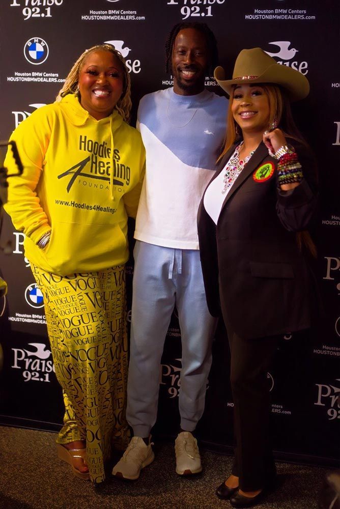 Three people are posing for a picture in front of a wall that says 92.1