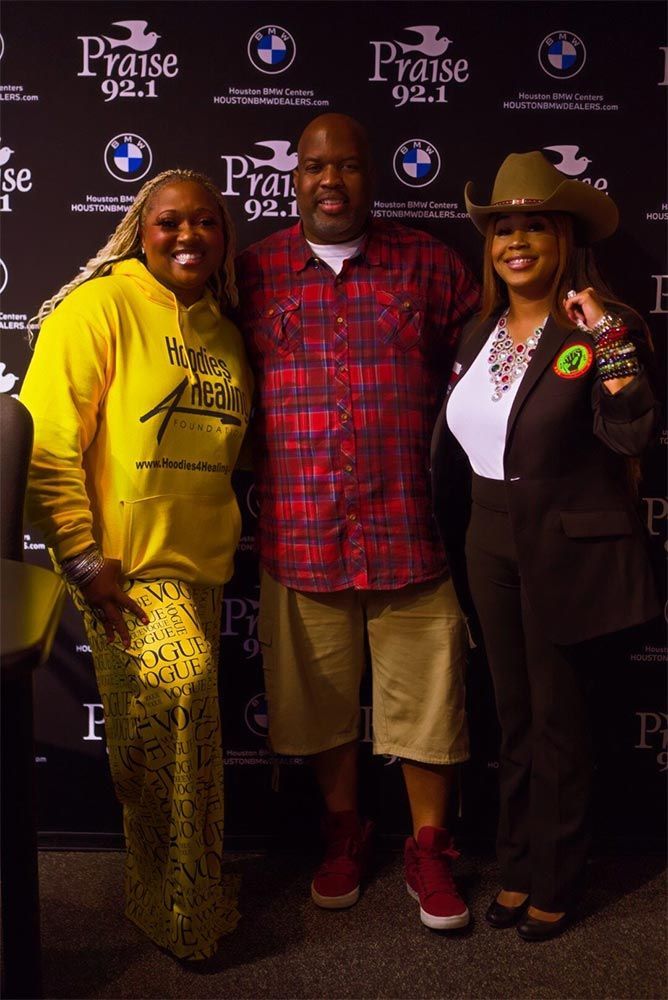 Three people posing for a picture in front of a wall that says praise 92.1