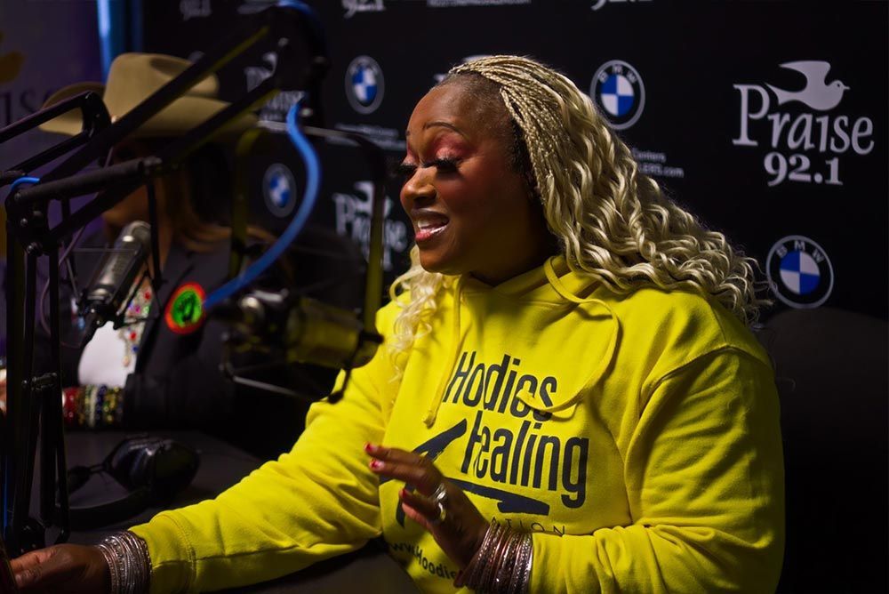 A woman in a yellow hoodie is sitting in front of a microphone.