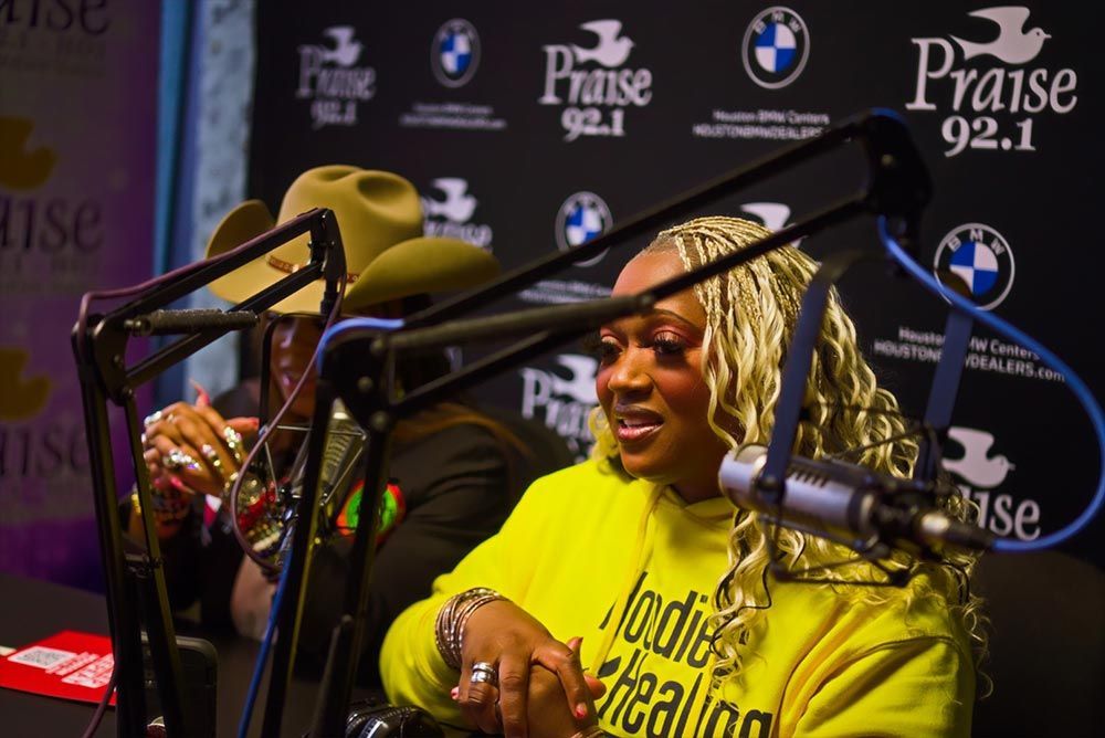 A woman in a yellow hoodie is sitting in front of a microphone.