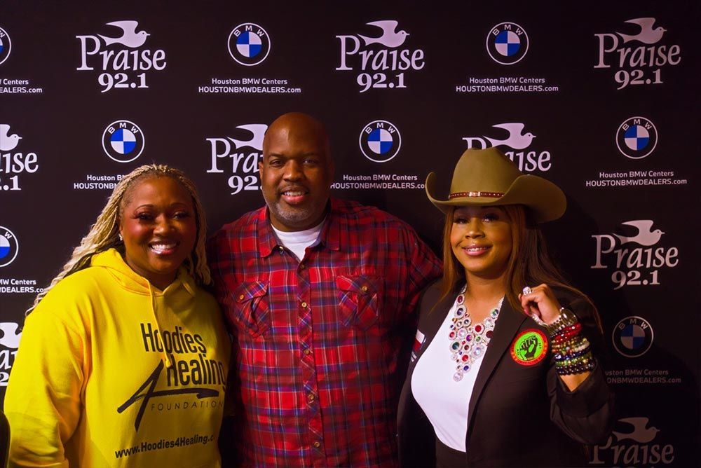 Three people are posing for a picture in front of a wall that says praise 92.1