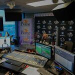 A man is sitting at a desk in front of a microphone in a control room.