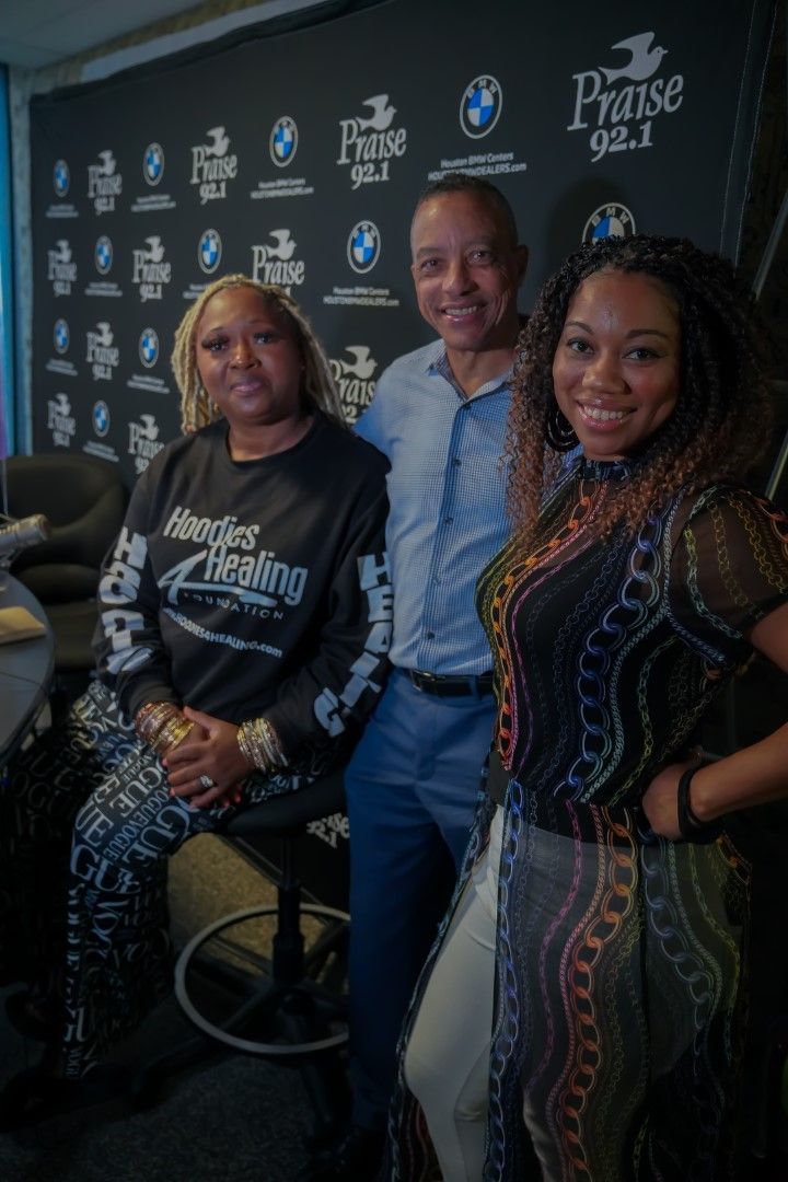 Three people are posing for a picture in front of a black wall.