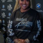 A woman wearing a black hoodie is sitting in front of a black wall.