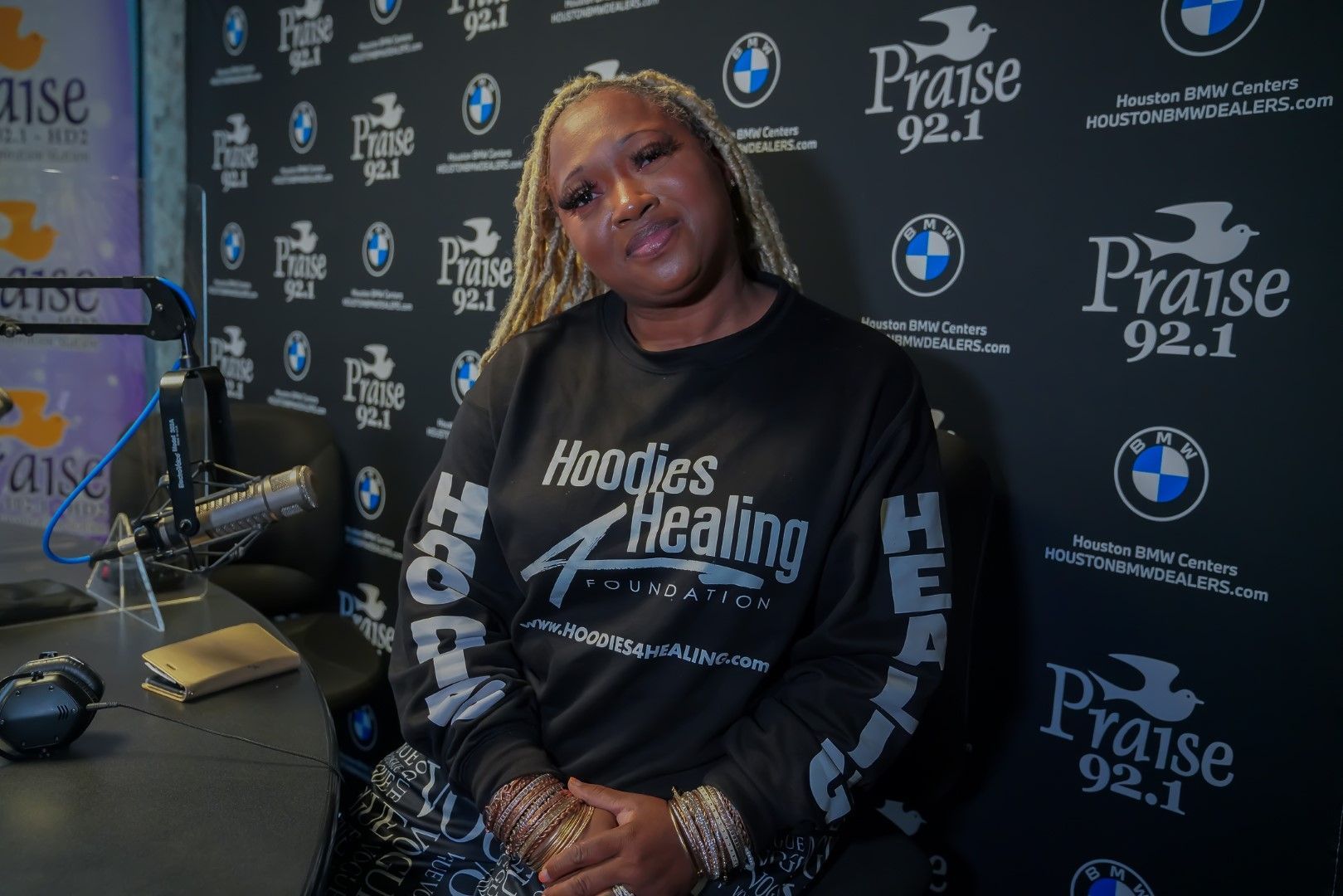 A woman is standing in front of a microphone wearing a hoodie.