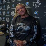 A woman is sitting in front of a black wall wearing a black shirt.