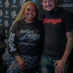 A man and a woman are standing next to each other in front of a black wall.