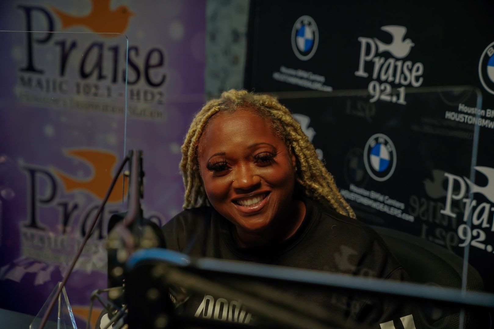 A woman is smiling in front of a sign that says praise