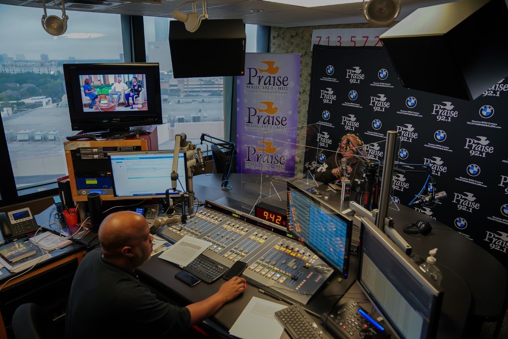 A man is sitting at a desk in front of a mixer in a radio station.
