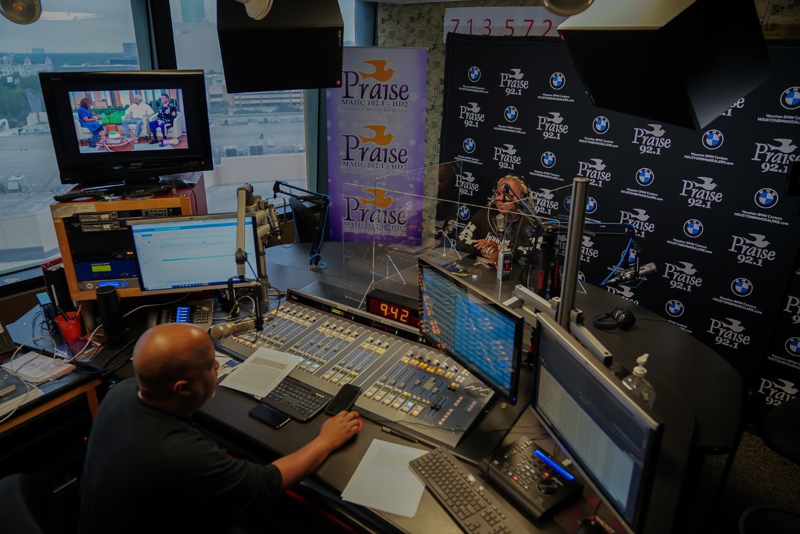 A man is sitting at a desk in front of a mixer in a radio station.