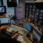 A man is sitting at a desk in front of a computer in a radio station.