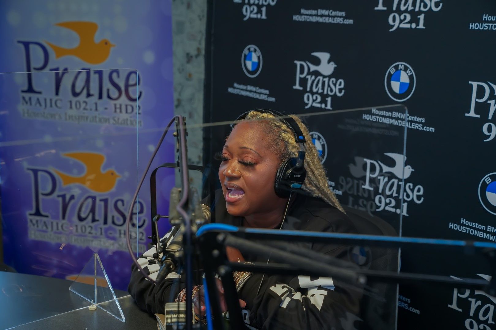A woman is singing into a microphone in front of a praise wall.