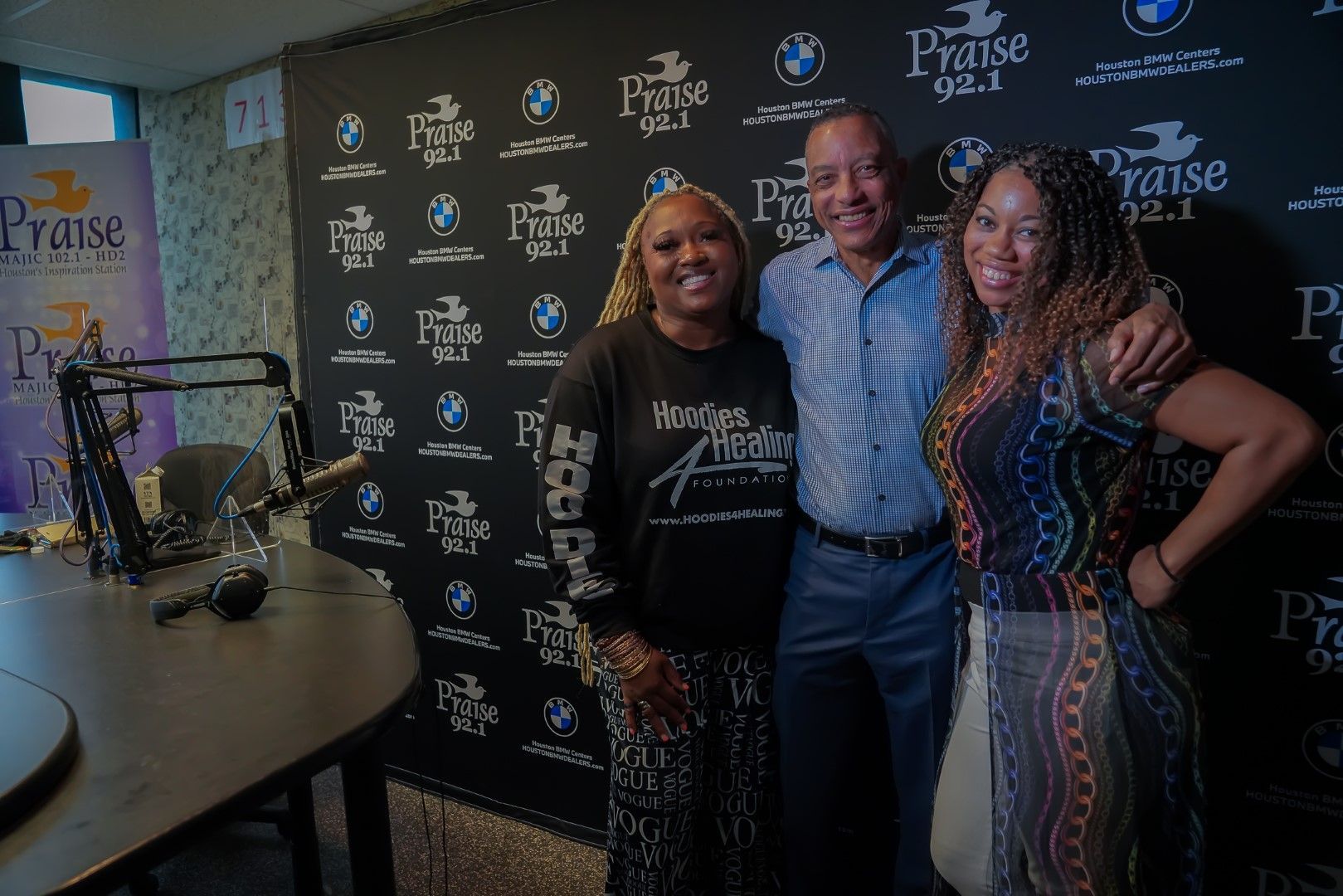A man and two women are posing for a picture in front of a microphone in a studio.