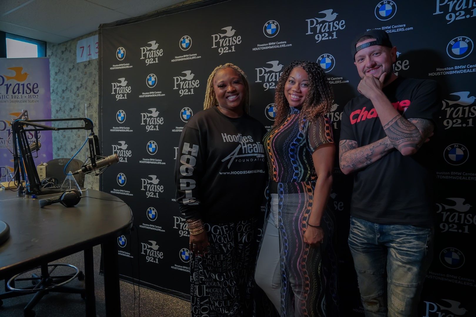 Three people are standing in front of a microphone in a studio.