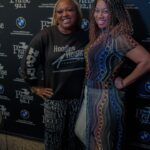 Two women are posing for a picture in front of a wall.